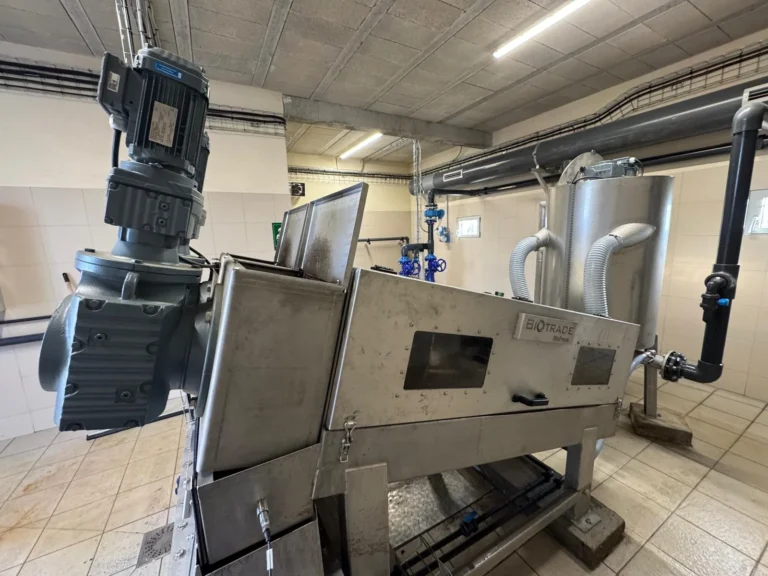 Presse à vis Biopress Biotrade installée dans une salle technique avec cuve de polymère et tuyauterie