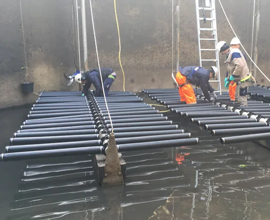 Techniciens en combinaison changeant des diffuseurs fines bulles sur rampes immergées dans un bassin d'aération en station d'épuration