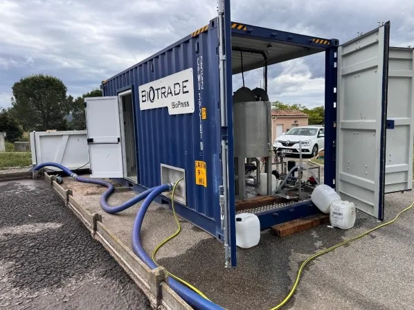 Conteneur mobile Biotrade Biopress bleu ouvert sur site avec presse à vis, tuyauteries et système de dosage de polymère lors d'un essai pilote