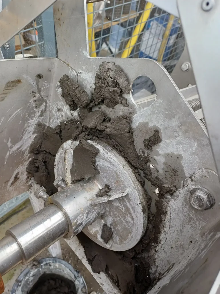 Gros plan sur la tête de sortie d'une presse à vis Biopress Biotrade avec gâteau de boues grises compactes lors d'un essai pilote